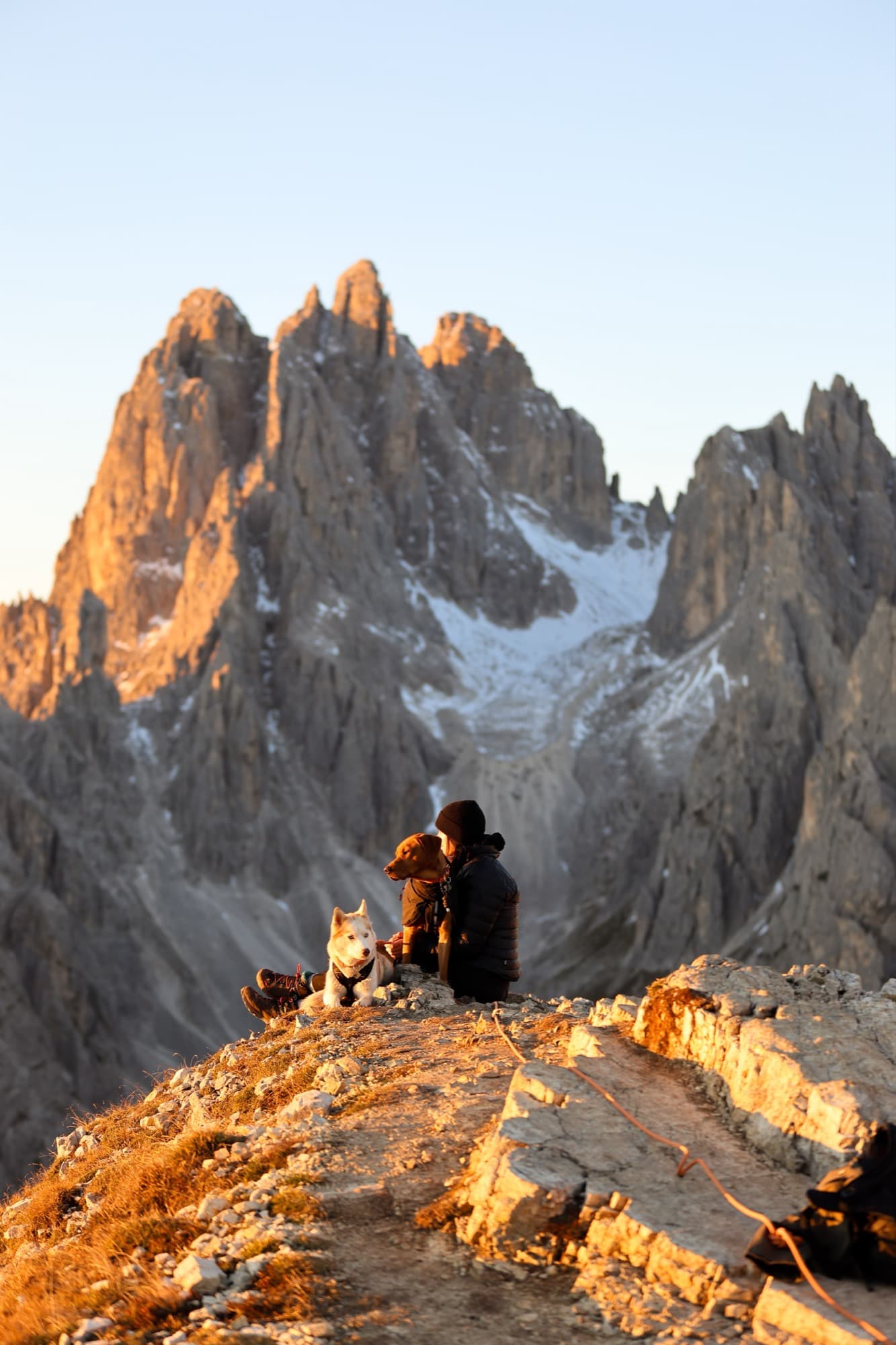 Robyn sitting with two dogs below jagged peaks at sunset